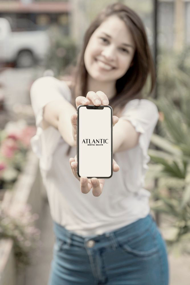 Happy student after receiving mental health holding a phone with Atlantic Mental Health Logo